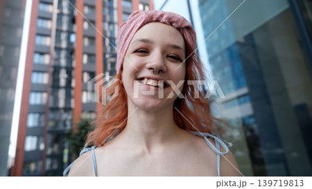 A teenage girl poses and smiles for a selfie on a smartphone. 139719813
