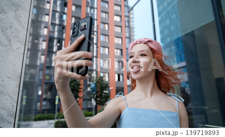 A teenage girl poses for a selfie on her smartphone. She shows her pierced tongue to her friends A teenage girl poses for a selfie on her smartphone. She shows her pierced tongue to her friends 139719893