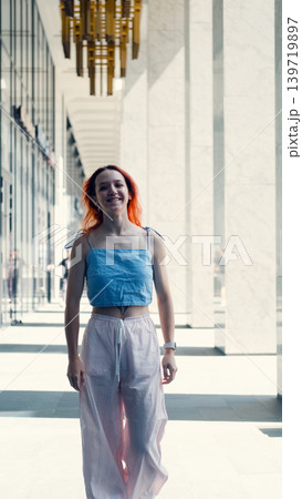 A portrait of a teenage girl with red hair posing for a photo near columns at the entrance to a business center 139719897