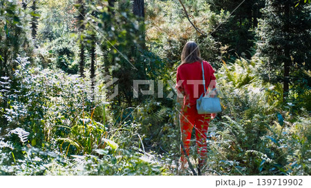 A girl on a walk, shot from behind. She's walking along a path in the arboretum, examining the plants A girl on a walk, shot from behind. She's walking along a path in the arboretum, examining the plants 139719902