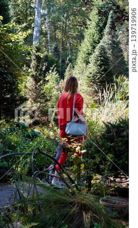 A girl on a walk, shot from behind. She's walking along a path in the arboretum, examining the plants 139719906