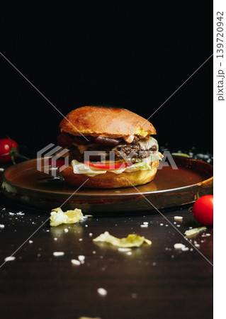 Dark backdrop shows burger on round wooden serving platter 139720942