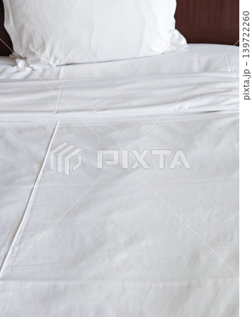 White bed linens with neatly arranged pillow on a bed in a hotel room, showcasing a clean and inviting sleeping environment 139722260