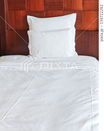 White bedding with a neatly arranged pillow on a wooden headboard in a modern bedroom setting, showcasing a clean and minimalist design aesthetic White bedding with a neatly arranged pillow on a wooden headboard in a modern bedroom setting, showcasing a clean and minimalist design aesthetic 139722262