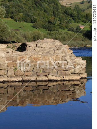 The ruins of an ancient rocky wall are reflected on the water surface of the river The ruins of an ancient rocky wall are reflected on the water surface of the river 139723413