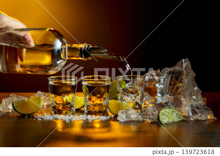 The tequila is poured from the bottle into shot glasses. 139723618