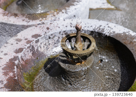 Ornate brass drinking fountain nozzle rises from a weathered stone basin 139723640