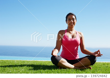 Grass, yoga and portrait of woman in lotus pose by water for holistic balance, mindfulness and exercise. Meditating, hands in prayer and person by ocean for wellness, health and zen energy outdoors Grass, yoga and portrait of woman in lotus pose by water for holistic balance, mindfulness and exercise. Meditating, hands in prayer and person by ocean for wellness, health and zen energy outdoors 139724842