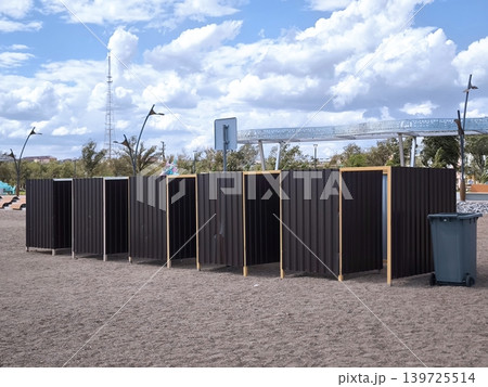 A row of dark changing cabins on a sandy beach under a cloudy sky A row of dark changing cabins on a sandy beach under a cloudy sky 139725514