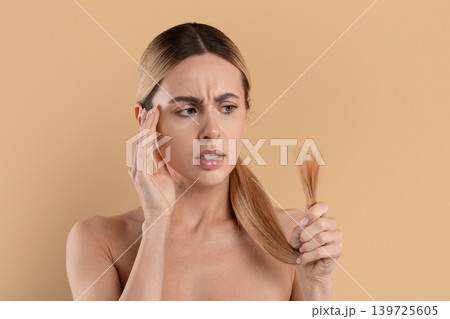 Worried young woman looking at damaged hair ends while checking hair condition 139725605