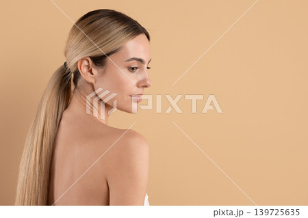 Young blonde woman with long ponytail turns back and looks over shoulder Young blonde woman with long ponytail turns back and looks over shoulder 139725635