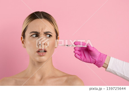 Nervous young woman reacting to cosmetic injection syringe near her face Nervous young woman reacting to cosmetic injection syringe near her face 139725644