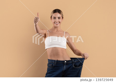 Slim young woman showing oversized jeans after successful weight loss Slim young woman showing oversized jeans after successful weight loss 139725649