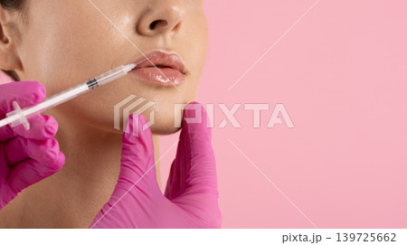 Woman receiving hyaluronic acid lip filler injection by doctor in pink gloves 139725662