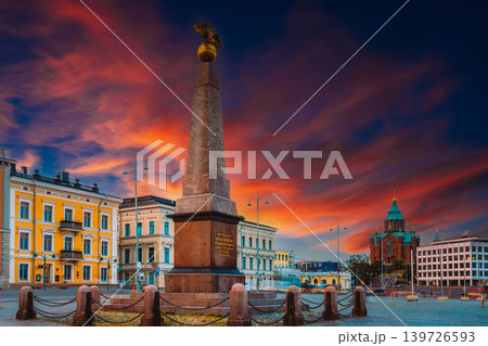 The Stone of the Empress (Keisarinnankivi) obelisk monument standing prominently in Market Square with historic buildings and the Uspenski Cathedral under a stunning sunset sky The Stone of the Empress (Keisarinnankivi) obelisk monument standing prominently in Market Square with historic buildings and the Uspenski Cathedral under a stunning sunset sky 139726593