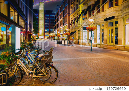 Helsinki, Finland. Bicycles Parked Near Storefronts In Kluuvikatu Street. Night Street In Kluuvi District In Evening Or Night Illumination. Quiet Pedestrian Street with Bicycles in Helsinki Helsinki, Finland. Bicycles Parked Near Storefronts In Kluuvikatu Street. Night Street In Kluuvi District In Evening Or Night Illumination. Quiet Pedestrian Street with Bicycles in Helsinki 139726660