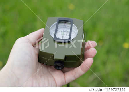 Magnetic liquid compass held in the palm of a hand, close-up against a green background. Device for navigation during hiking, trekking Magnetic liquid compass held in the palm of a hand, close-up against a green background. Device for navigation during hiking, trekking 139727132