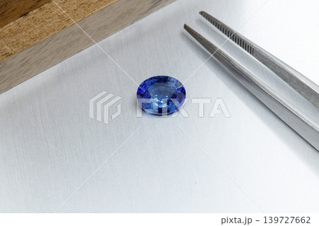 macro mineral faceted stone sapphire with tweezers on a gray background macro mineral faceted stone sapphire with tweezers on a gray background 139727662