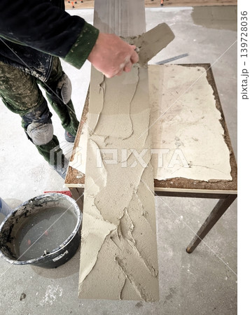 A builder applies cement adhesive to a long porcelain tile. 139728036