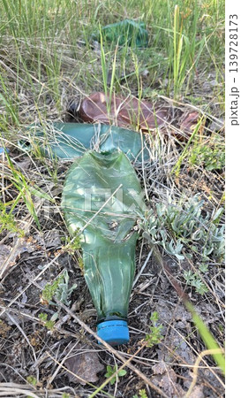 Crushed empty green and brown plastic bottles abandoned in dry grass and soil on a summer day, concept of environmental pollution and littering Crushed empty green and brown plastic bottles abandoned in dry grass and soil on a summer day, concept of environmental pollution and littering 139728173