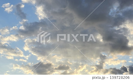 Blue sky with dramatic dark grey and fluffy white clouds illuminated by warm sunlight at sunset or sunrise, concept of weather changes and heaven 139728206