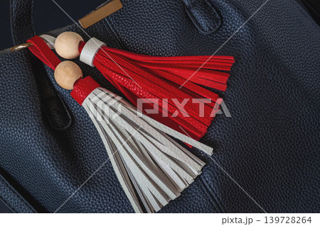 Leather tassels with wooden beads hang on black handbag surface with pebbled texture. Fashion tassel detail, bag decor, leather craft, handmade style, accessory design Leather tassels with wooden beads hang on black handbag surface with pebbled texture. Fashion tassel detail, bag decor, leather craft, handmade style, accessory design 139728264