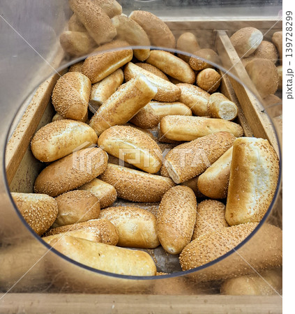 Golden bread buns with sesame seeds are displayed in a transparent plastic container at a grocery store. Customers can easily view the fresh baked goods. Golden bread buns with sesame seeds are displayed in a transparent plastic container at a grocery store. Customers can easily view the fresh baked goods. 139728299