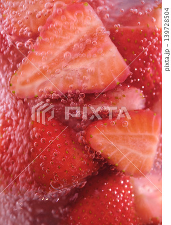 Strawberry slices in fizzy drink are seen against a bubble-filled background in a glass during bright daylight hours Strawberry slices in fizzy drink are seen against a bubble-filled background in a glass during bright daylight hours 139728504