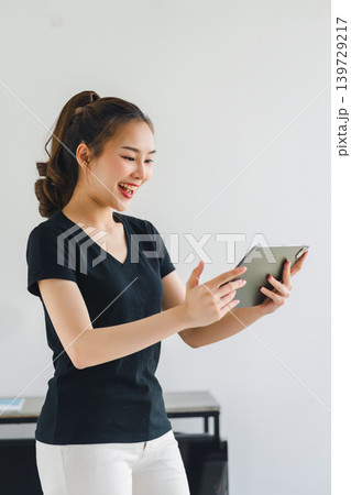 Confident asian woman with friendly smile stands with hand holding digital tablet isolated on white background. 139729217
