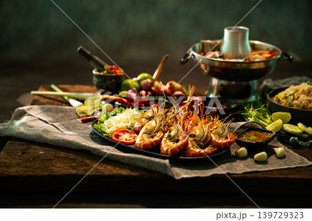 Authentic Thai seafood feast with grilled river prawns, spicy dipping sauce, fresh herbs and traditional hot pot served on rustic wooden table in warm gourmet restaurant atmosphere Authentic Thai seafood feast with grilled river prawns, spicy dipping sauce, fresh herbs and traditional hot pot served on rustic wooden table in warm gourmet restaurant atmosphere 139729323