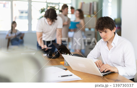 Guy sitting at desk is working on laptop computer. 139730337