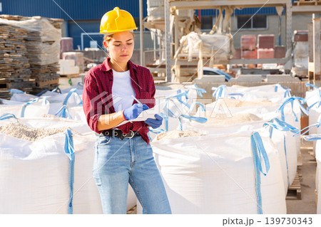 Woman manager keeps records of sandbags in the open area of construction store Woman manager keeps records of sandbags in the open area of construction store 139730343
