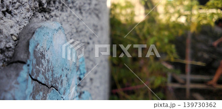 Close up of blue paint cracks on a concrete wall against a natural blurry background. 139730362