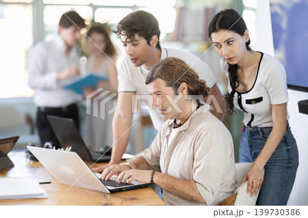 Colleagues looking at one laptop together in office Colleagues looking at one laptop together in office 139730386