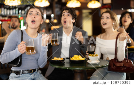 Group of emotive young friends supporters cheering for favorite team celebrating victory with glasses of alcohol in beer pub Group of emotive young friends supporters cheering for favorite team celebrating victory with glasses of alcohol in beer pub 139730393
