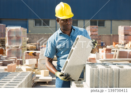 Man holding hollow concrete brick in hands in outdoor warehouse Man holding hollow concrete brick in hands in outdoor warehouse 139730411