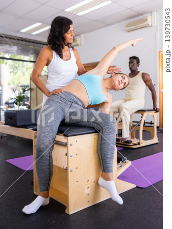 Woman trainer teaching young woman to do body stretching at pilates workout closeup Woman trainer teaching young woman to do body stretching at pilates workout closeup 139730543