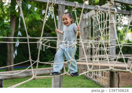 preschool child girl playing and walking on wooden rope bridge at outdoor playground in park preschool child girl playing and walking on wooden rope bridge at outdoor playground in park 139730628