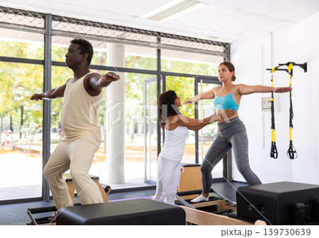 Man and woman doing exercises in pilates gym with man instructor Man and woman doing exercises in pilates gym with man instructor 139730639