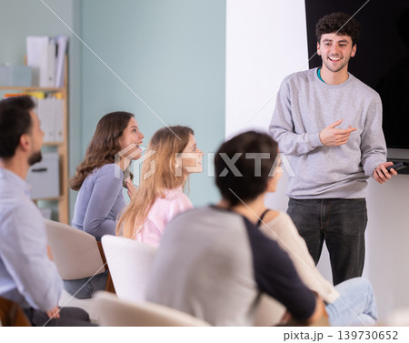 Male lecturer communicates with students, controls projector using remote control. Male lecturer communicates with students, controls projector using remote control. 139730652