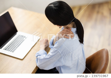 リビングでパソコン作業をしながら肩に手を当てて痛そうな表情をする日本人女性 139731967