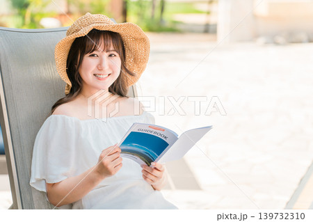 プールサイドのリクライニングチェアに座りガイドブックを読む若いアジア人女性 139732310