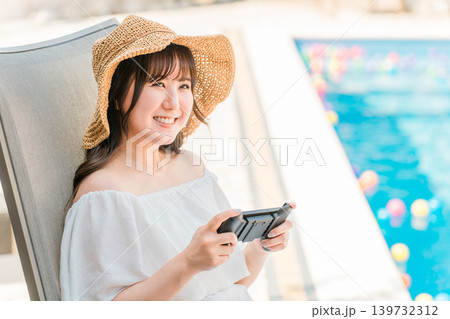プールサイドでリクライニングチェアに座りゲームをする若いアジア人女性 プールサイドでリクライニングチェアに座りゲームをする若いアジア人女性 139732312