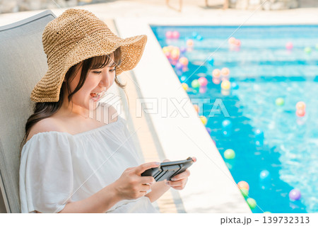 プールサイドでリクライニングチェアに座りゲームをする若いアジア人女性 139732313