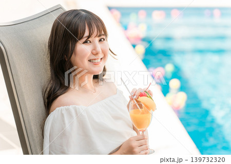 プールサイドのリクライニングチェアに座りトロピカルジュースを飲む若いアジア人女性 プールサイドのリクライニングチェアに座りトロピカルジュースを飲む若いアジア人女性 139732320
