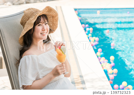 プールサイドのリクライニングチェアに座りトロピカルジュースを飲む若いアジア人女性 139732323