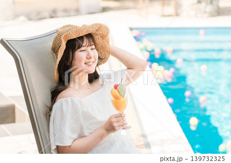 プールサイドのリクライニングチェアに座りトロピカルジュースを飲む若いアジア人女性 プールサイドのリクライニングチェアに座りトロピカルジュースを飲む若いアジア人女性 139732325