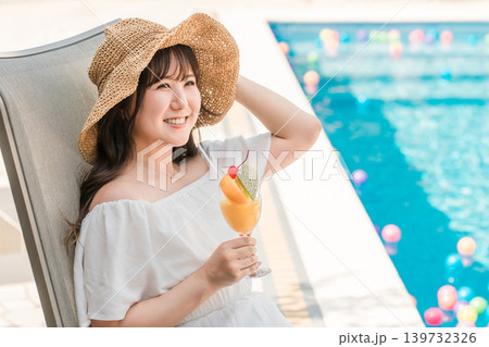 プールサイドのリクライニングチェアに座りトロピカルジュースを飲む若いアジア人女性 プールサイドのリクライニングチェアに座りトロピカルジュースを飲む若いアジア人女性 139732326