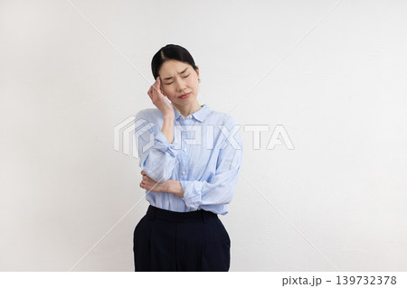 白い壁の前でこめかみに手を当てて痛そうな表情をする日本人女性 白い壁の前でこめかみに手を当てて痛そうな表情をする日本人女性 139732378