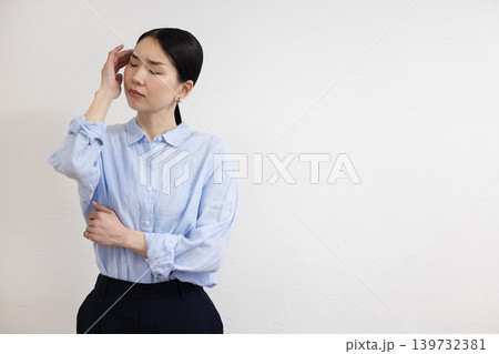 白い壁の前でこめかみに手を当てて痛そうな表情をする日本人女性 139732381